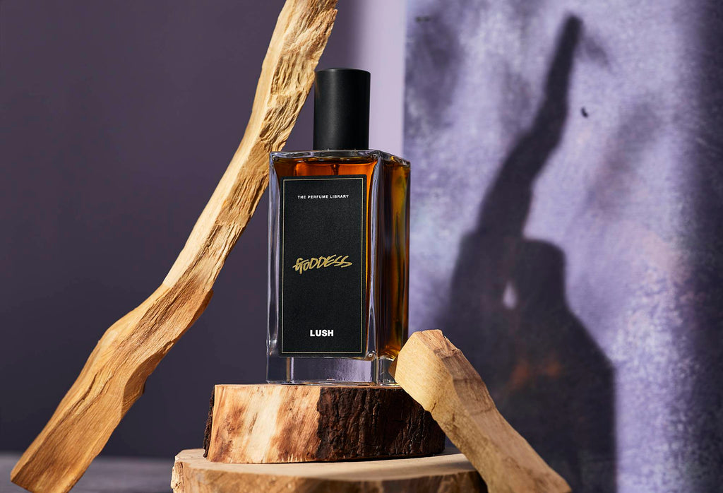 A dark amber coloured bottled perfume, Goddess, sits on top of a display of sandalwood, one of it's main ingredients.
